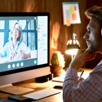 Serious male student wearing headphones taking online course training, watching webinar, remote university class, virtual learning with social distance web teacher, tutor or coach using computer.