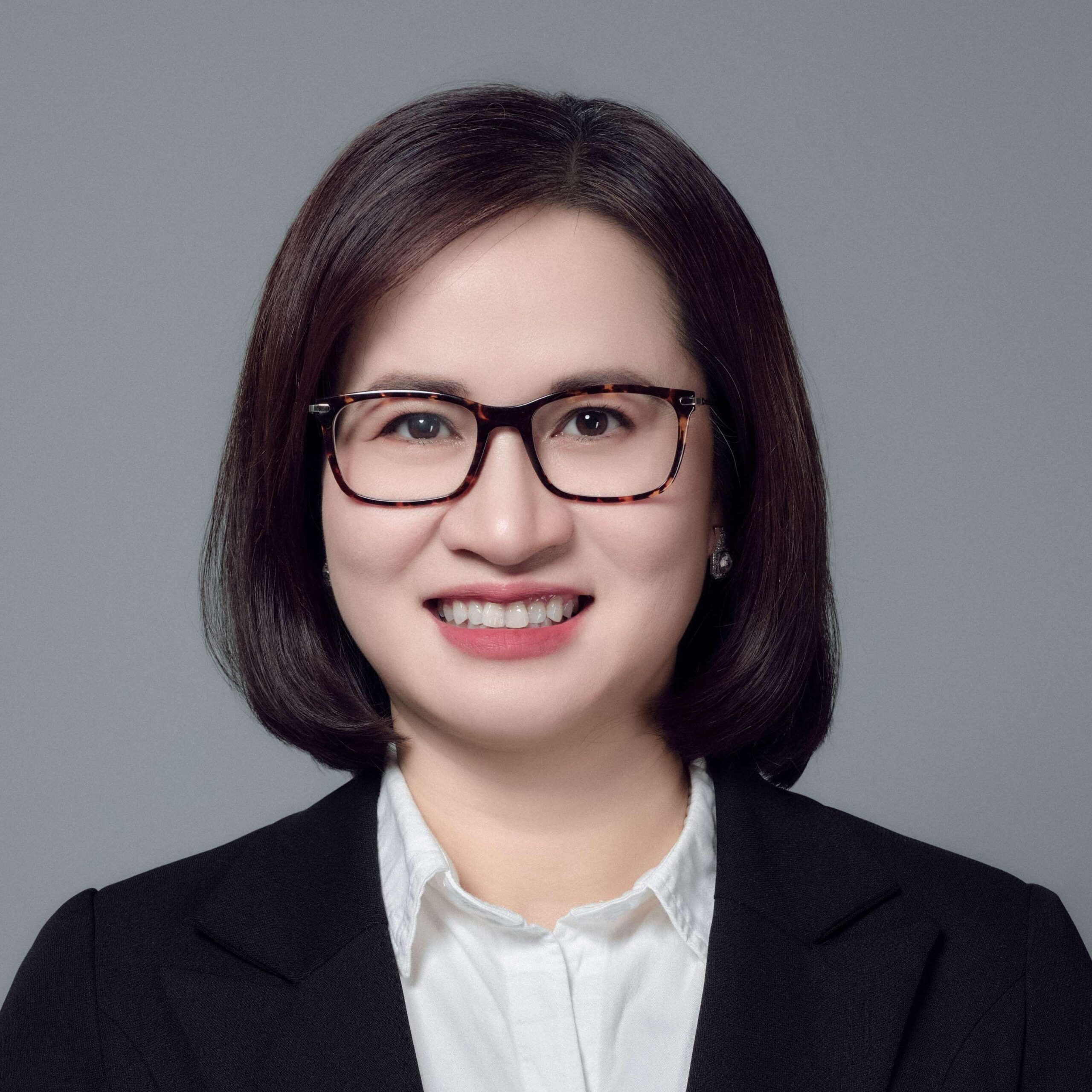 This is the headshot of an award winner smiling with dark glasses, a black blazer and white button down shirt in front of a grey background.