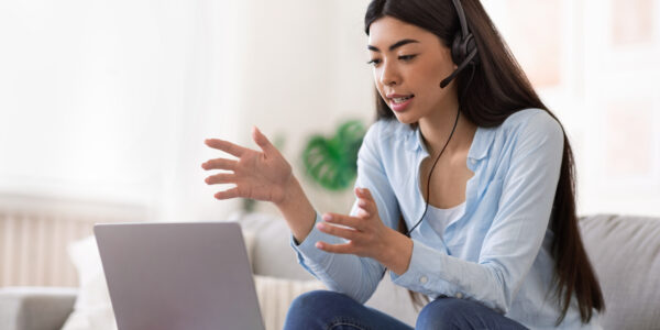 Online Tutoring. Young asian female tutor having video call with students, talking at laptop camera, sitting on couch at home