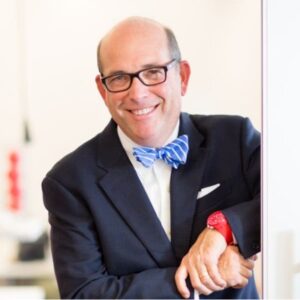 Smiling headshot of award winner in front of a mostly white background wearing a blue and white bow tie and a navy blue suit jacket.